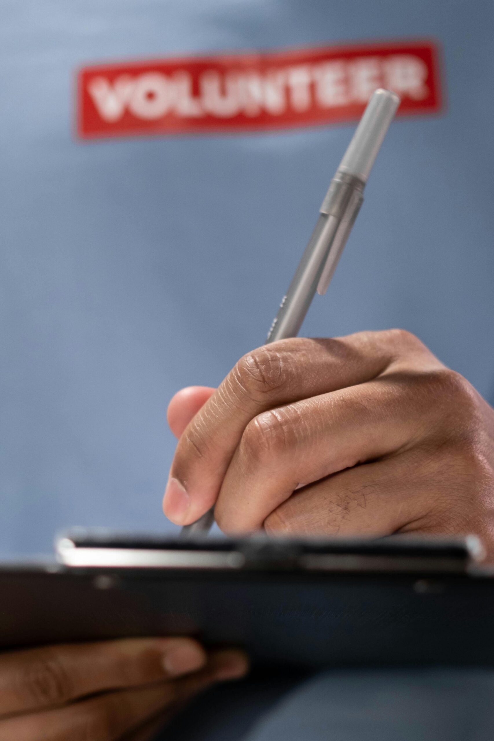 A volunteer in a blue shirt writes on a clipboard, highlighting community service.