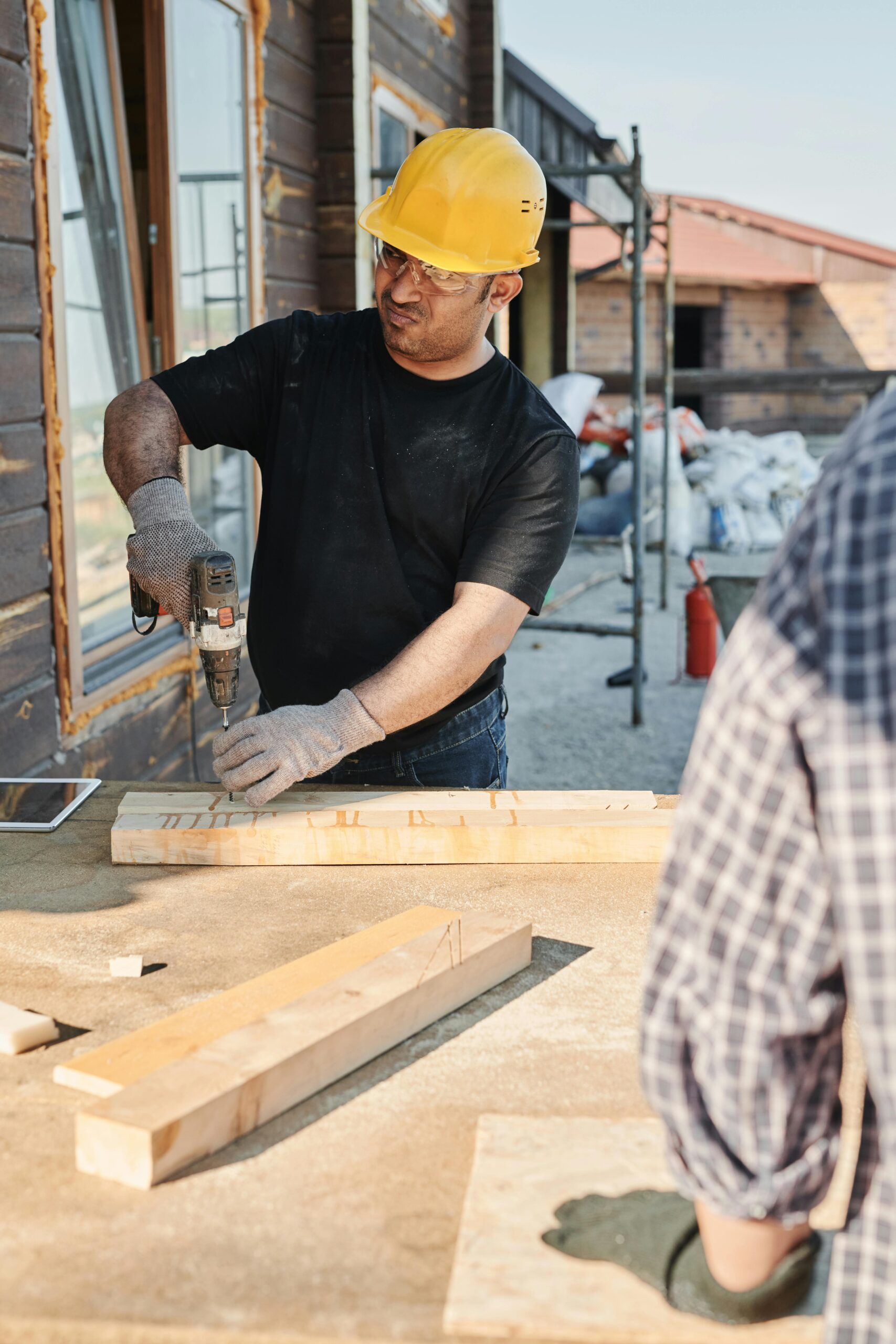 A construction worker using a drill on wood at a building site outdoors.
